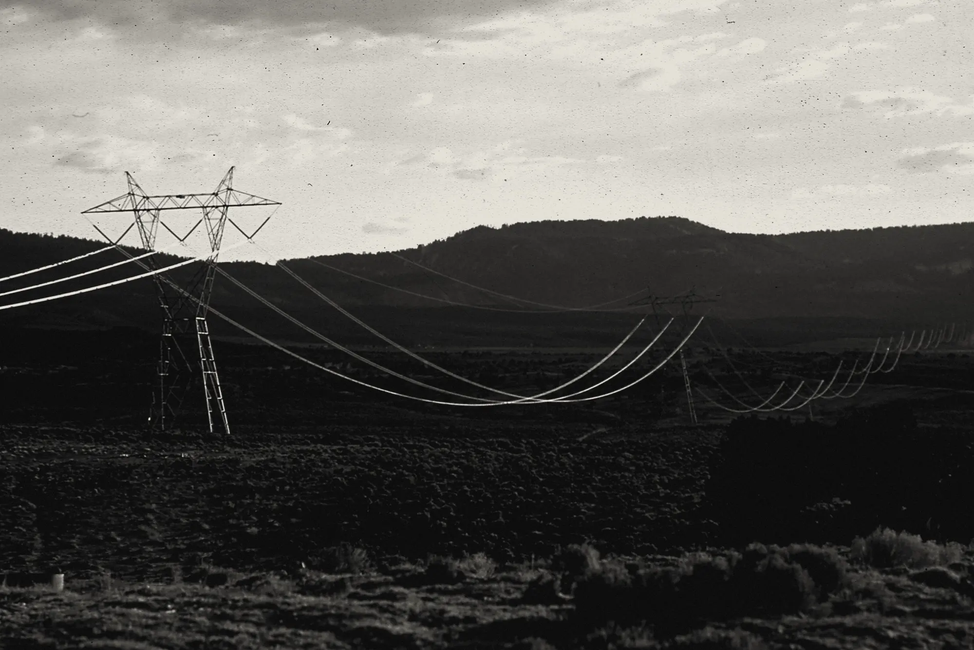 A transmission line crossing high desert toward the horizon at dusk