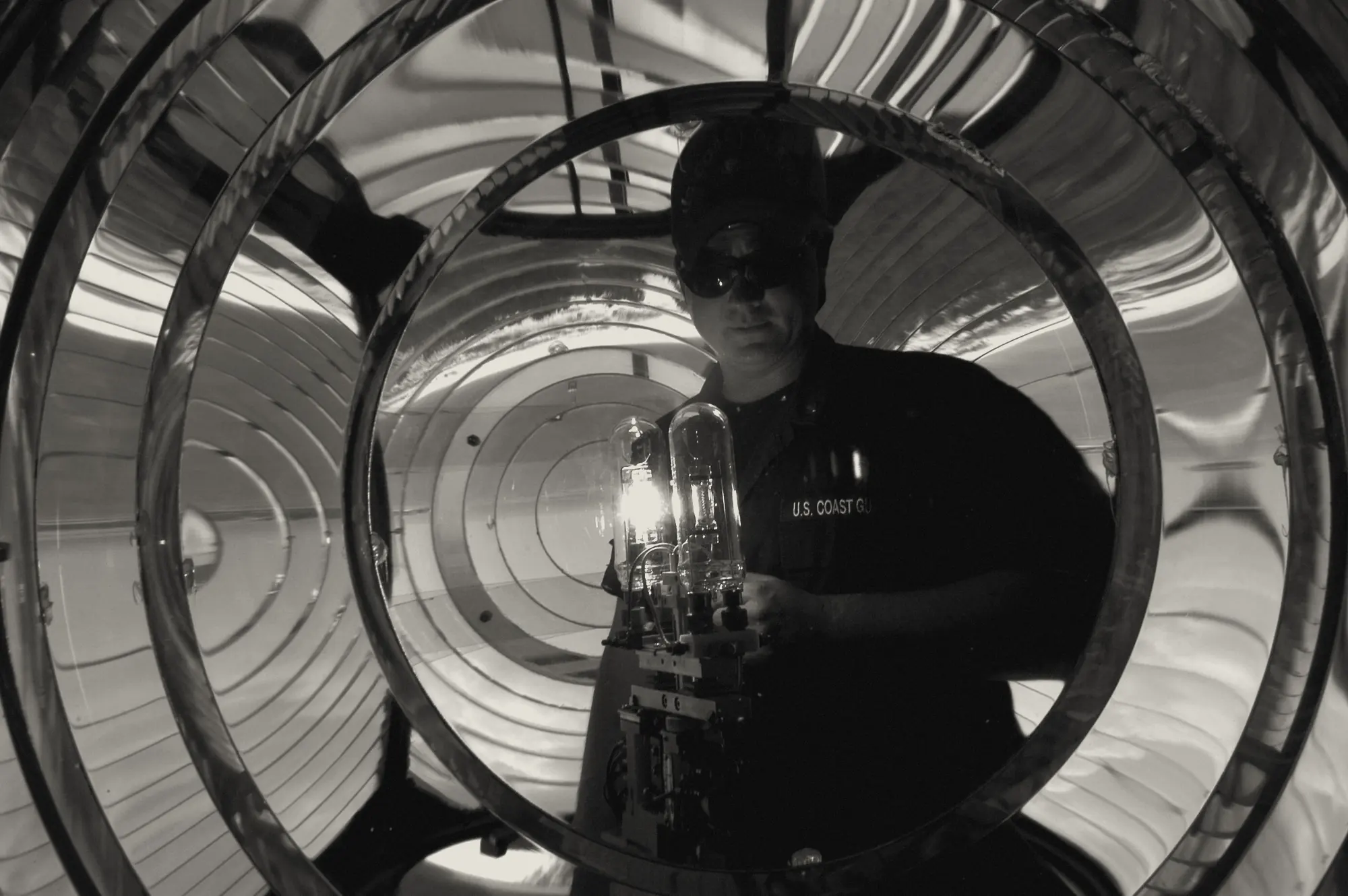 A Coast Guard keeper testing a lamp at the center of a lighthouse's Fresnel lens