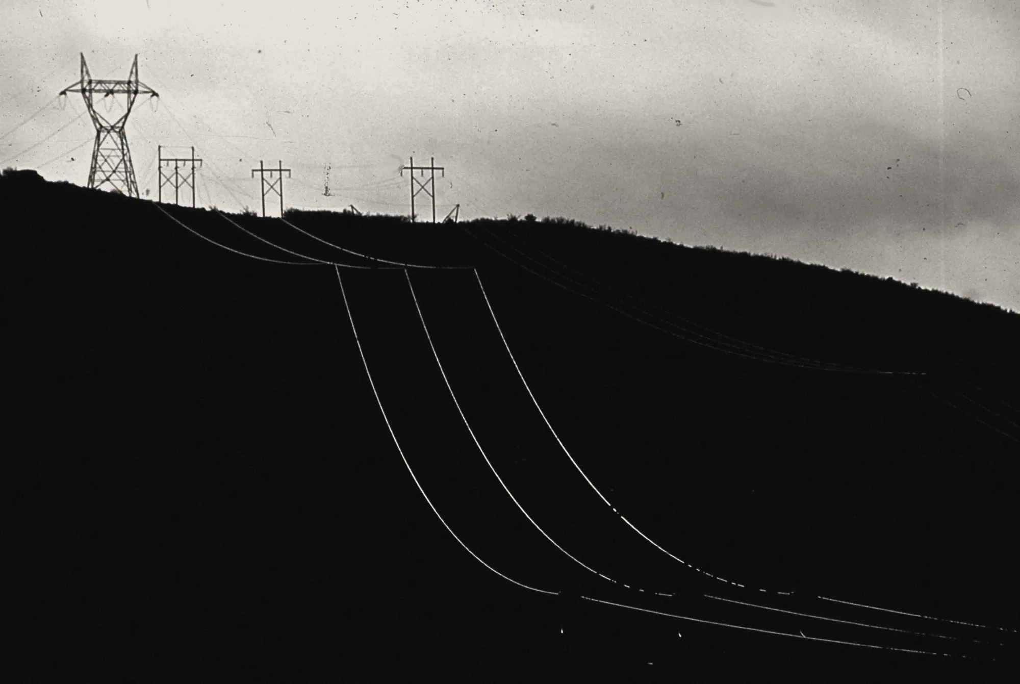 High-voltage lines catching the last light as they cross a dark ridge